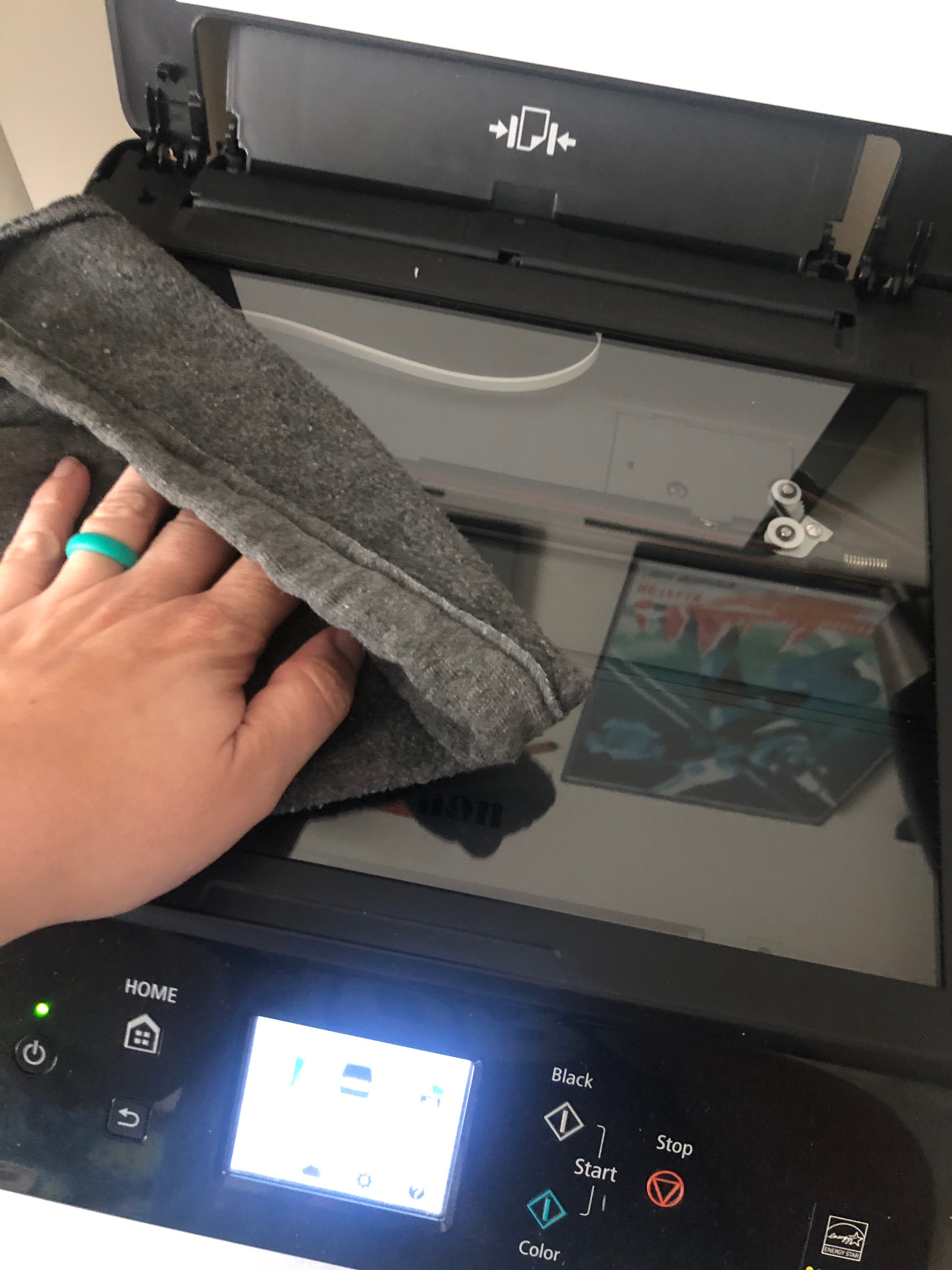 A hand wiping a scanner glass with a cloth to clean it before scanning a sketch, ensuring a clear scan for digital artwork preparation.