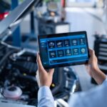 Mechanic using a diagnostic tablet to inspect a car engine, highlighting the use of technology in modern vehicle repair.