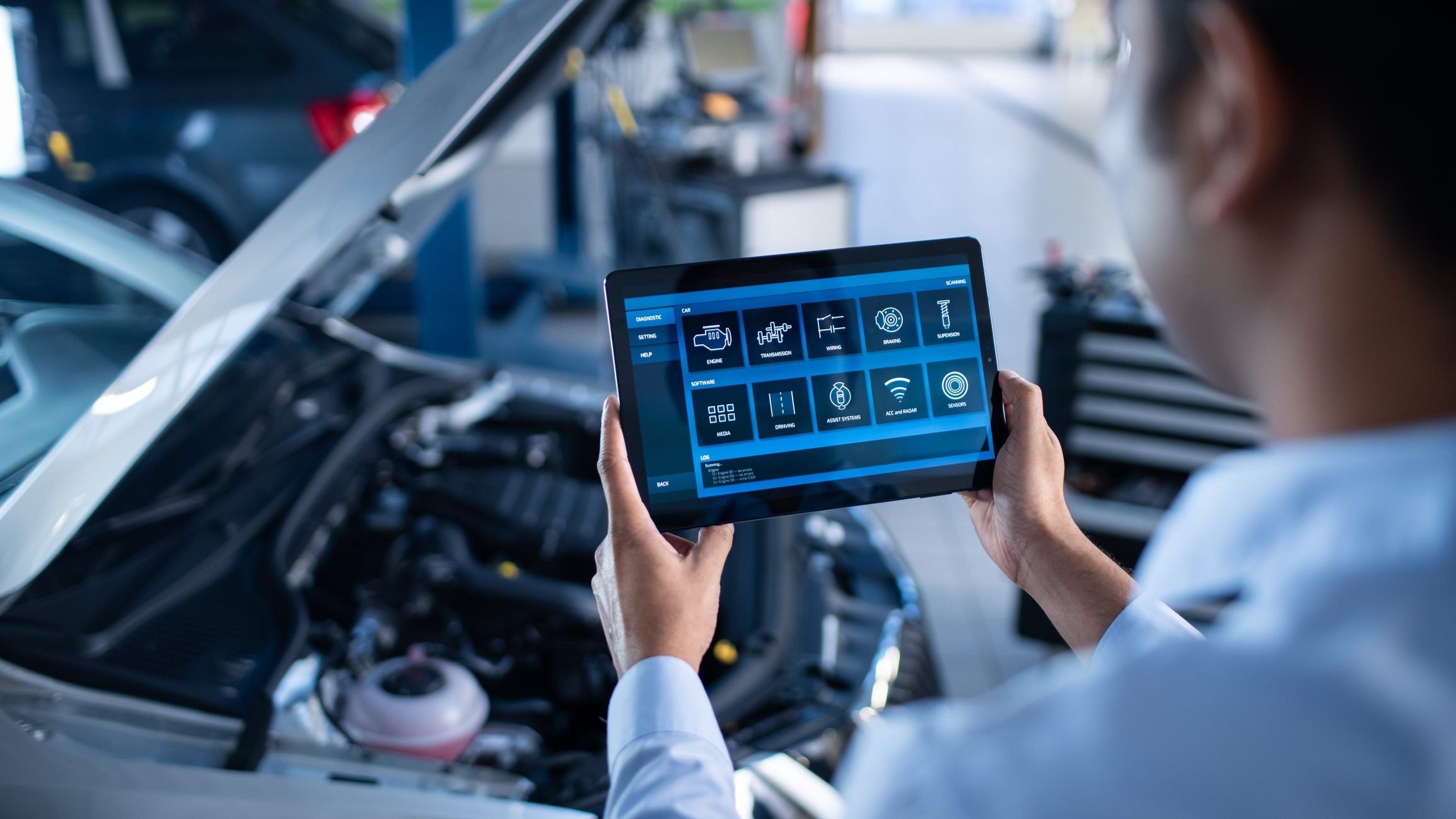 Mechanic using a diagnostic tablet to inspect a car engine, highlighting the use of technology in modern vehicle repair.