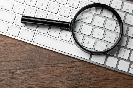 A magnifying glass over a keyboard inspecting website accessibility